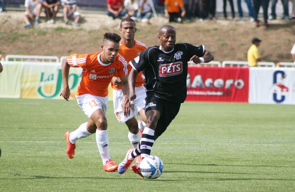 Jean Michel Boucicaut lleva el balon ante la defensa de dos jugadores del Cibao FC